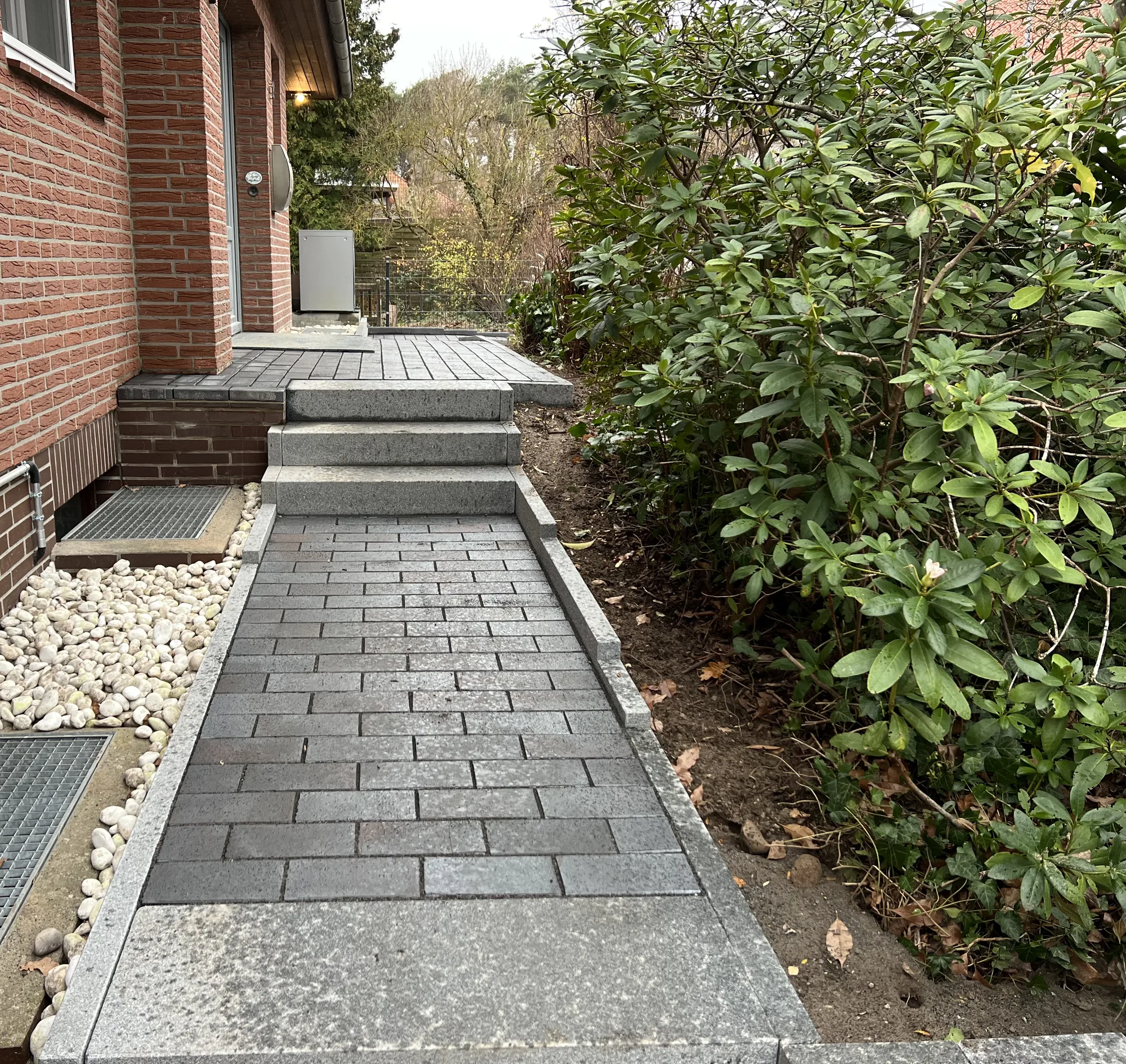 Neuer Pflasterweg mit Granit-Blockstufen zur Haustür, weiße Kiesstreifen an der Fassade